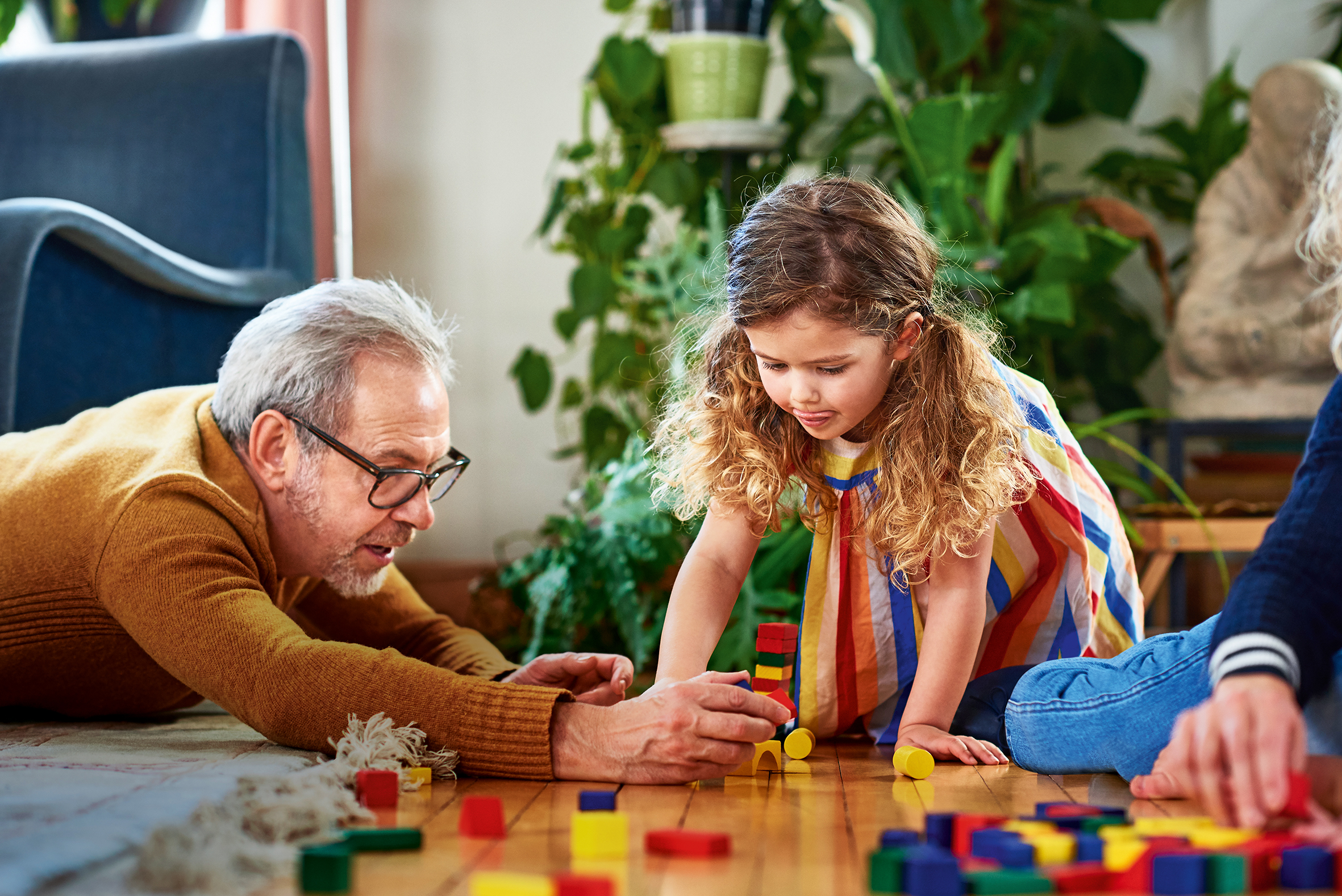 Mature man and young girl playing with wooden blocks on wooden floor, building tower, balance, care, concentration
